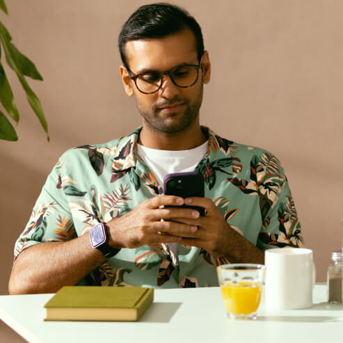 Bir adam kafedeki bir masada oturuyor, akıllı telefonundaki uygulamadan Wise hesabını kontrol ediyor.